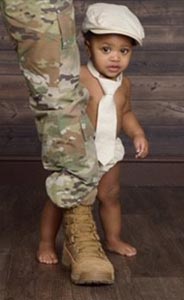Toddler stands behind his dad in an army uniform