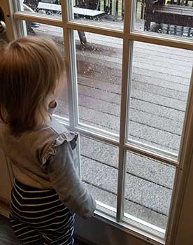 Toddler girl looking out the door at the snow falling