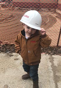 3 year-old with construction hat on holding his hat