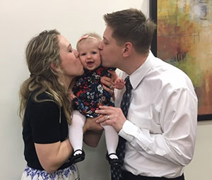 Adoptive parents each kissing baby girl on a cheek