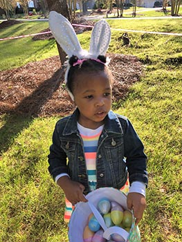 Little black girl wearing bunny ears on an Easter egg hunt