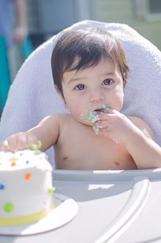 One year old boy with hand in cake and cake on face