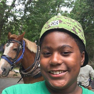 Black boy in green hat poses with a horse behind him