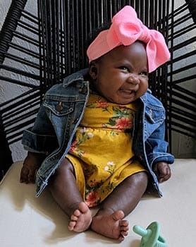cute black baby girl happily sitting in a chair looking at Mom