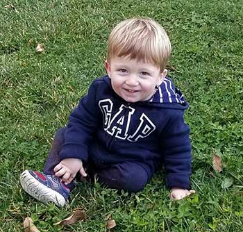 happy baby sits on grass and smiles at camera
