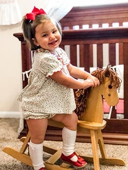 Young toddler laughs as she rocks on her wooden rocking horse