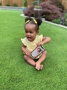 baby enjoys time on the grass and shows off her baby photo on mom's phone