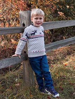 Leo at four years old stands by a fence and smiles for photo