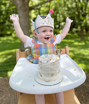 Lucie celebrating her first Birthday with glee, frosting all over her arms and a crown on her head
