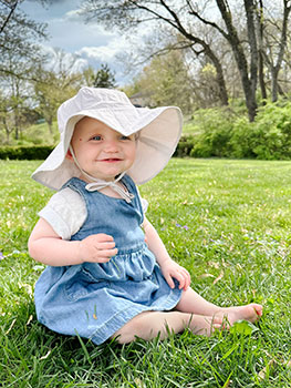 Lucie sitting in the grass with her sun hat and smiling